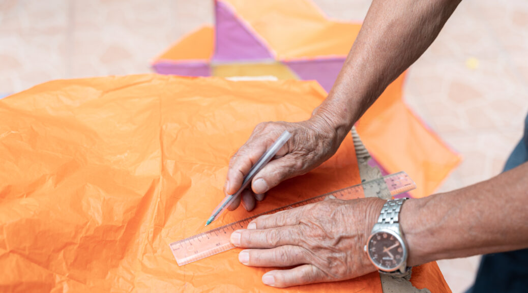 A senior Hispanic man is measuring papier mache to create a Day of the Dead lamp